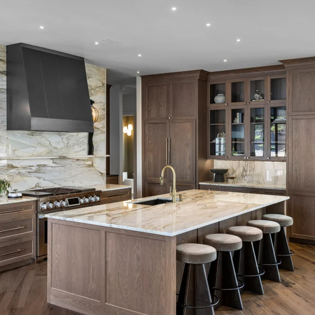 Kitchen with dark hood, marble wall and stainless range beside walnut island in The Sanctuary by Mike Stevens Homes