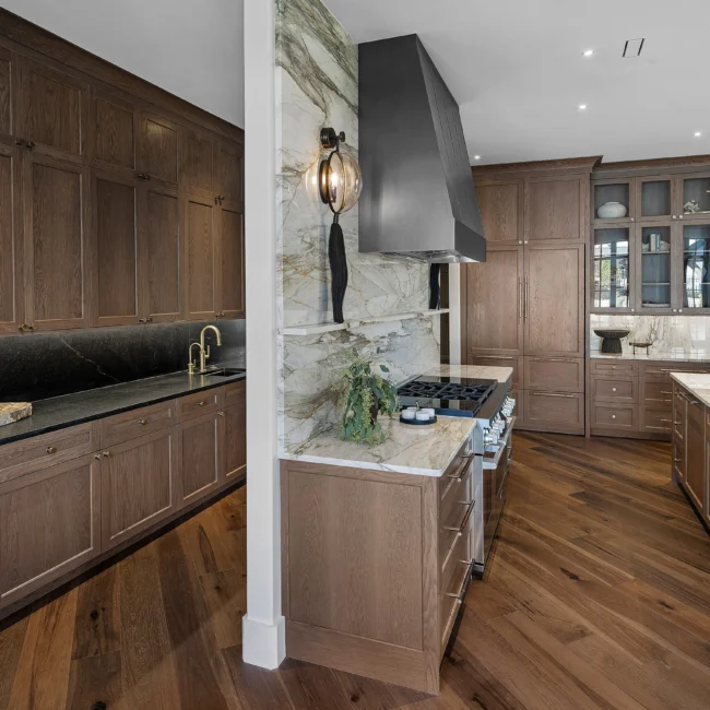 Kitchen with stone range wall, black hood and tall walnut pantry cabinets in The Sanctuary by Mike Stevens Homes