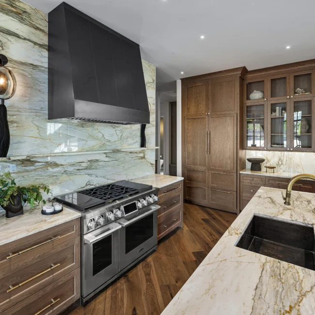 Range and marble backsplash beneath black hood with gold pulls on walnut cabinets in The Sanctuary by Mike Stevens Homes