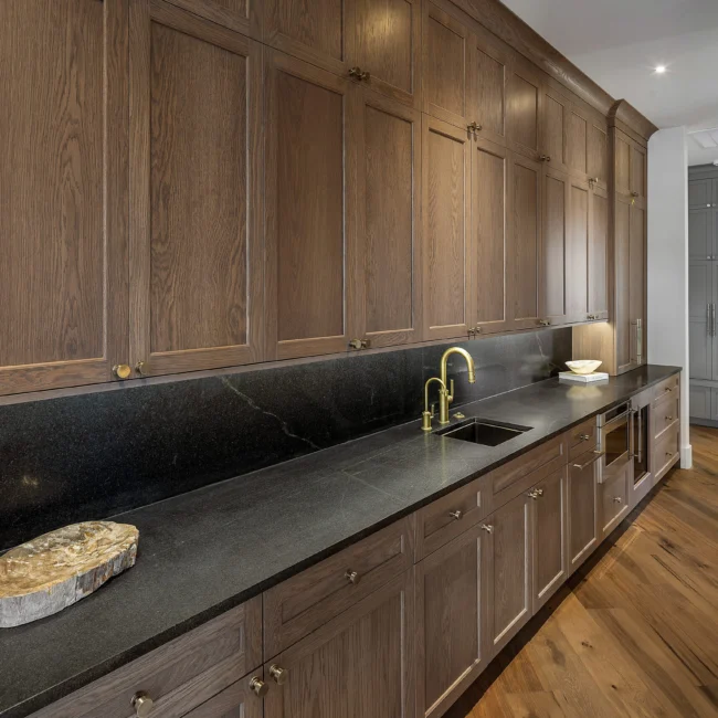Long galley kitchen with black honed countertops and walnut upper cabinets in The Sanctuary by Mike Stevens Homes
