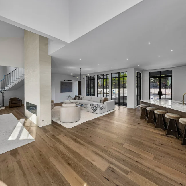 Open great room with wide-plank oak floors, black-framed windows and staircase in The Sanctuary by Mike Stevens Homes