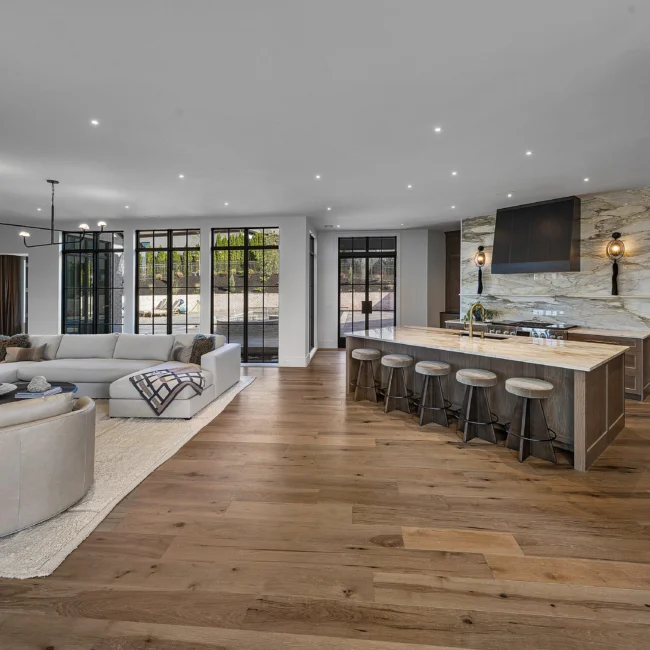 Great room with black-framed windows, sectional seating and bar stools at island in The Sanctuary by Mike Stevens Homes