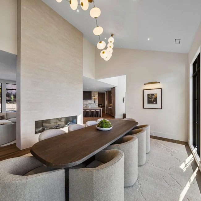 Dining table with curved upholstered chairs and linear fireplace in The Sanctuary by Mike Stevens Homes