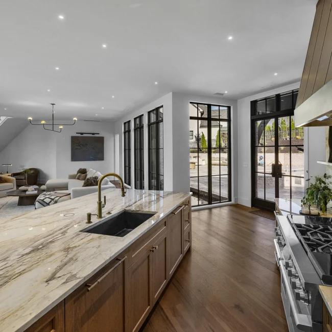 Kitchen sink with marble counter and black windows opening to backyard in The Sanctuary by Mike Stevens Homes