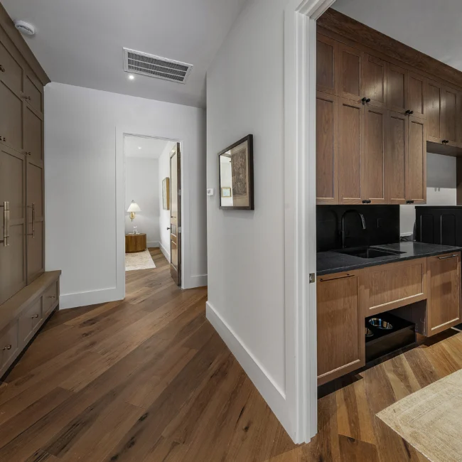 Hallway with wood cabinetry, wet bar sink and framed art in The Sanctuary by Mike Stevens Homes