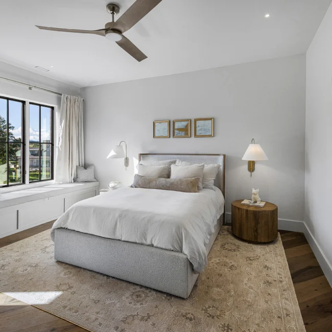 Guest bedroom with upholstered gray bed, window seat and wall sconces in The Sanctuary by Mike Stevens Homes