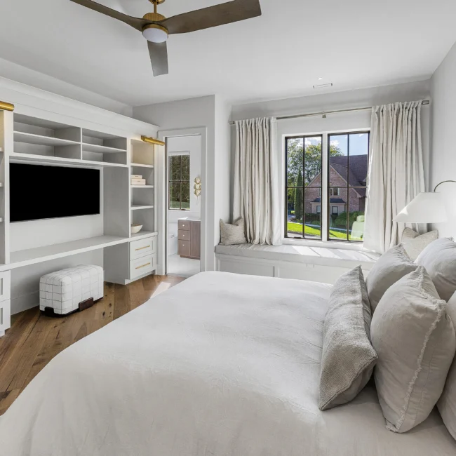 Bedroom with built-in media wall, white bed and window seat in The Sanctuary by Mike Stevens Homes