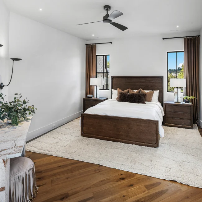 Primary bedroom with dark wood bed, white linens and neutral rug in The Sanctuary by Mike Stevens Homes