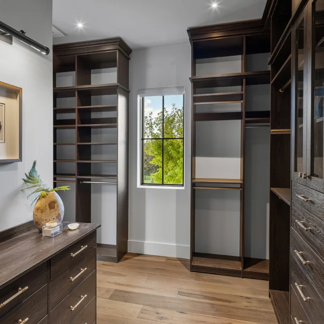 Walk-in closet with dark wood cabinetry, shelving and window in The Sanctuary by Mike Stevens Homes