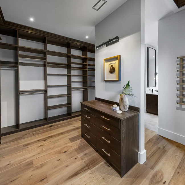Walk-in closet with island dresser and open wood shelving in The Sanctuary by Mike Stevens Homes