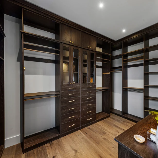 Walk-in closet with glass-front cabinets and drawer banks in The Sanctuary by Mike Stevens Homes