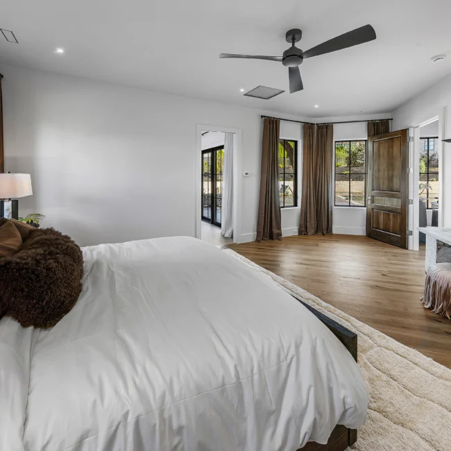 Primary suite bedroom with ceiling fan, wood floors and white bedding in The Sanctuary by Mike Stevens Homes