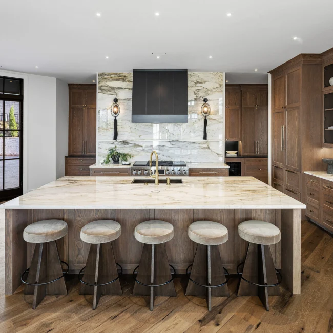 Kitchen island with five bar stools below marble hood and walnut cabinets in The Sanctuary by Mike Stevens Homes