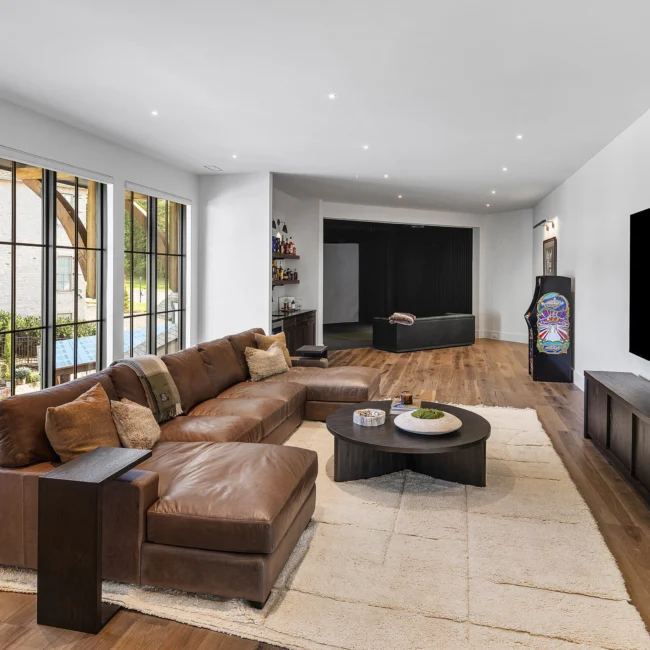 Living room with brown leather sectional, round coffee table and bar in The Sanctuary by Mike Stevens Homes