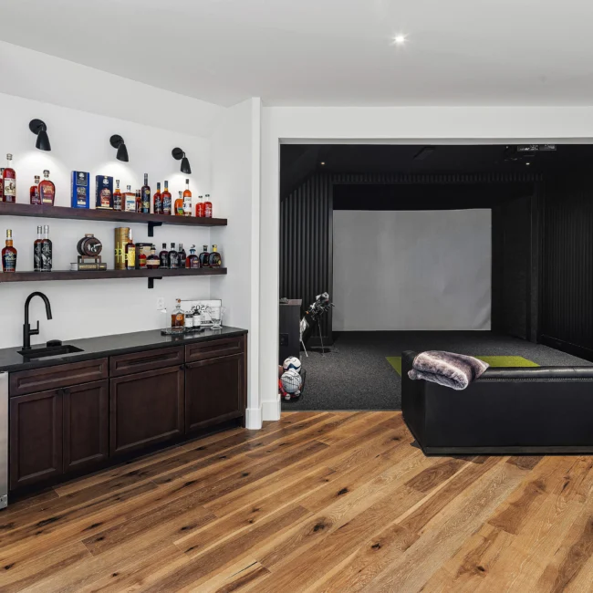 Wet bar with glass shelves of liquor bottles facing a home theater screen in The Sanctuary by Mike Stevens Homes