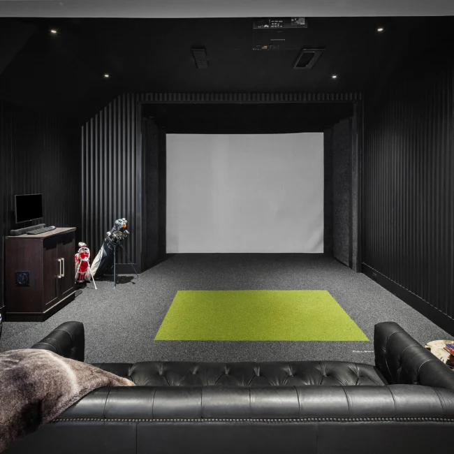 Home theater with projection screen, green rug and black leather sofa in The Sanctuary by Mike Stevens Homes