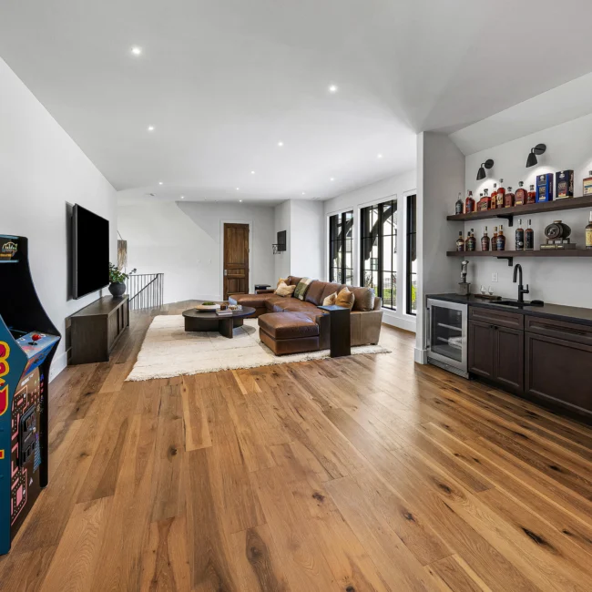 Game room with arcade cabinet, leather sectional and open wet bar in The Sanctuary by Mike Stevens Homes
