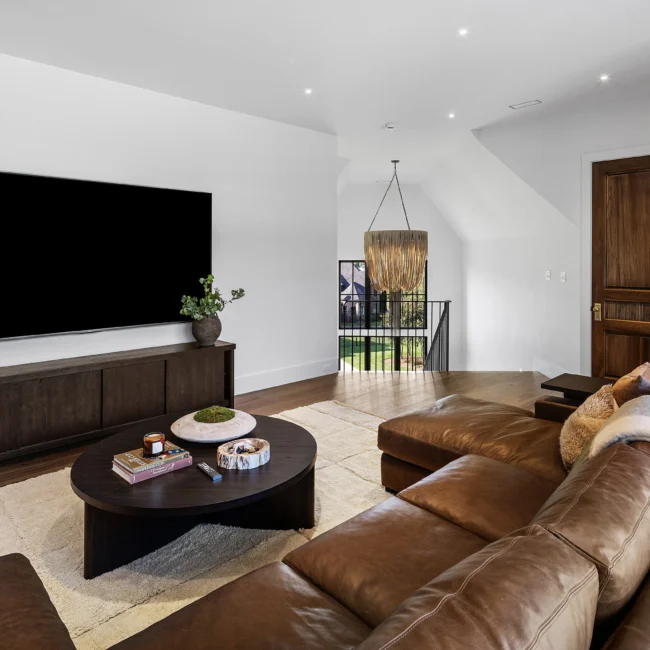 Media room with wall-mounted TV, brown leather sofa and round coffee table in The Sanctuary by Mike Stevens Homes
