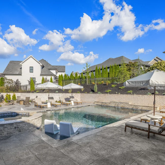 Backyard pool with lounge chairs, gray stone patio and white umbrellas in The Sanctuary by Mike Stevens Homes