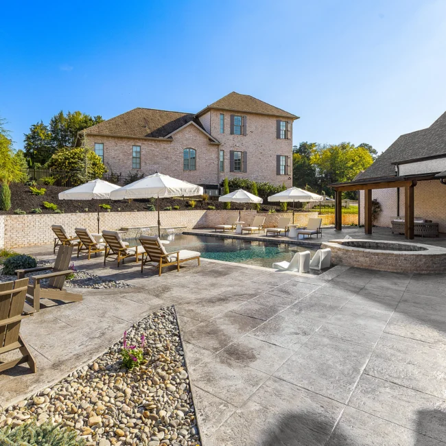 Pool deck with wood lounge chairs, umbrellas and spa beside brick home in The Sanctuary by Mike Stevens Homes