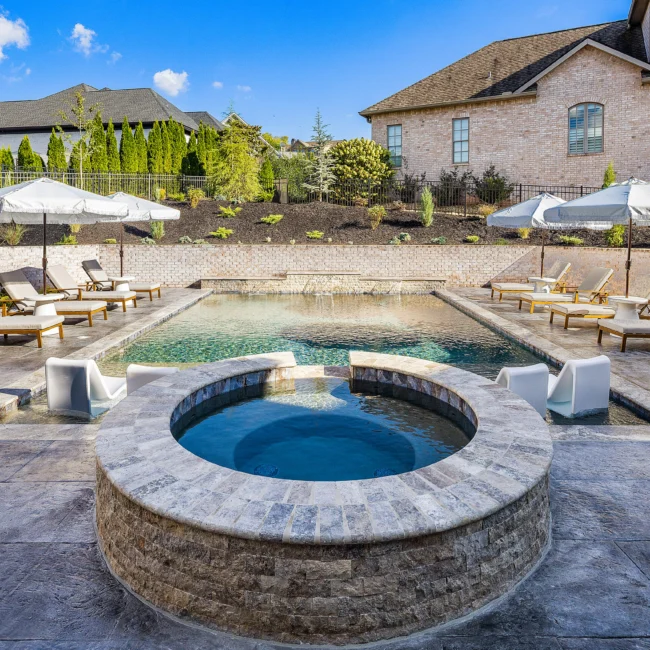 Round stone spa with blue water beside pool and white lounge chairs in The Sanctuary by Mike Stevens Homes