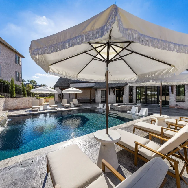Pool and patio with large cream umbrella, lounge chairs and outdoor living room in The Sanctuary by Mike Stevens Homes