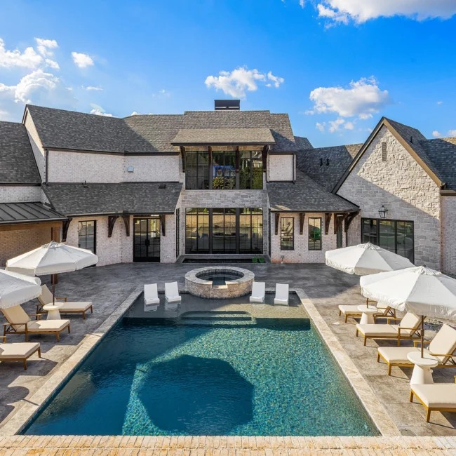 Back patio with rectangular pool, fire bowl and cream umbrellas in The Sanctuary by Mike Stevens Homes