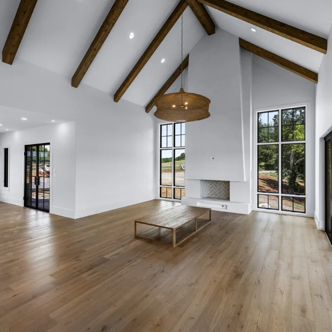 Vaulted living room with timber beams, wood floors and tall windows in Edgewater Estate, a custom home by Mike Stevens Homes