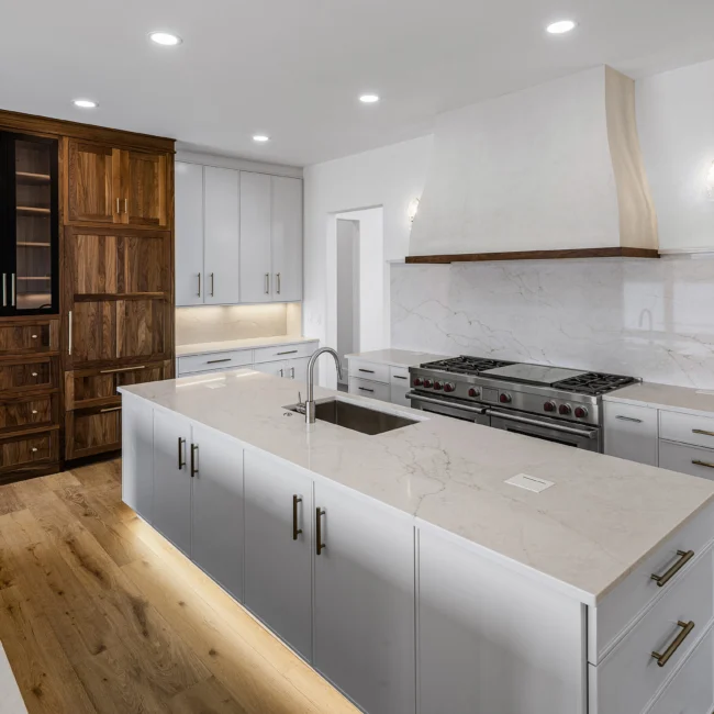 White kitchen with quartz island, vent hood and pro gas range in Edgewater Estate, a custom home by Mike Stevens Homes