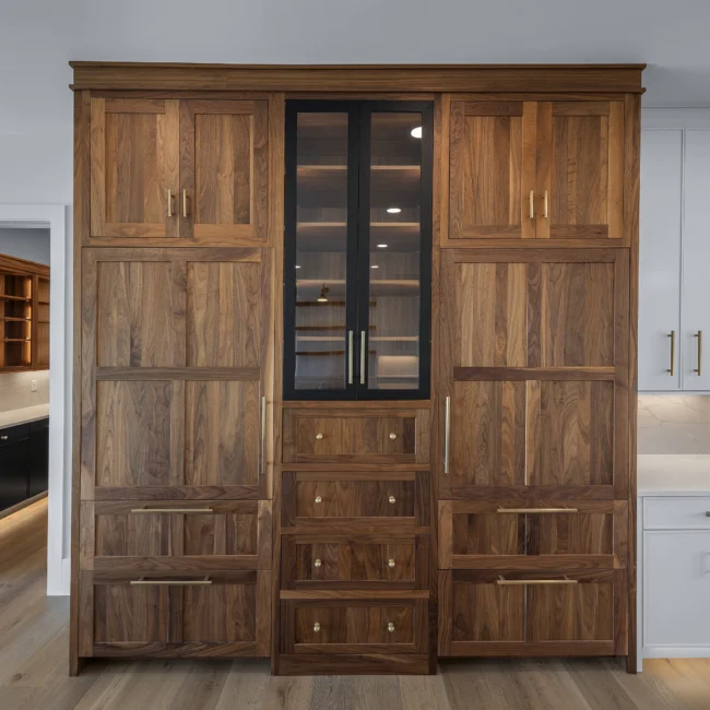 Walnut pantry wall with glass-front cabinet and paneled drawers in Edgewater Estate, a custom home by Mike Stevens Homes