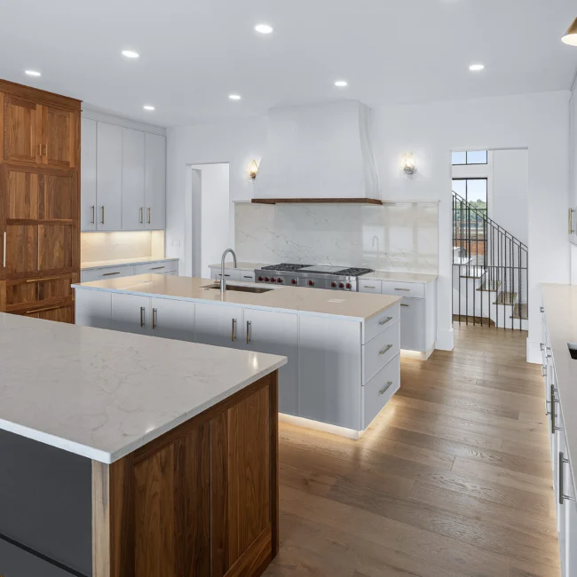 Open kitchen with white hood, gray island and staircase in view in Edgewater Estate, a custom home by Mike Stevens Homes