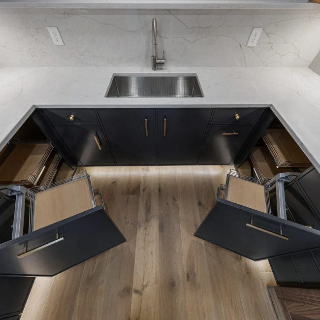 Gray base cabinets with open pull-out drawers and brass pulls in Edgewater Estate, a custom home by Mike Stevens Homes
