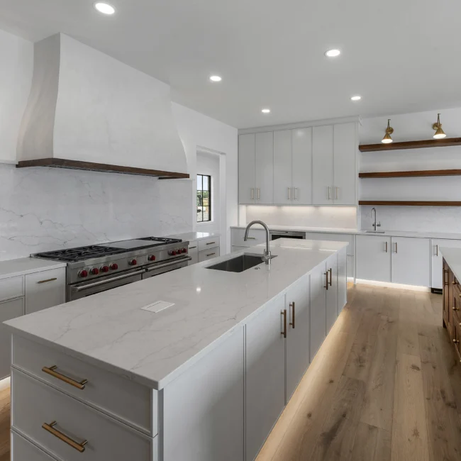 White kitchen with quartz island, vent hood and open walnut shelves in Edgewater Estate, a custom home by Mike Stevens Homes