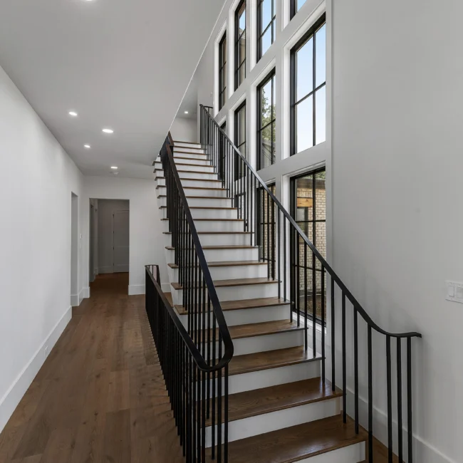 Staircase with black iron railing, wood treads and tall windows in Edgewater Estate, a custom home by Mike Stevens Homes