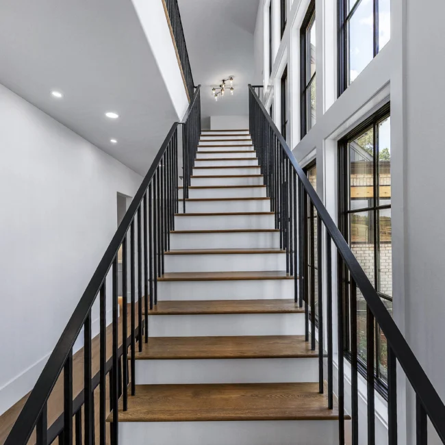 Open-tread staircase with black iron balusters and two-story windows in Edgewater Estate, a custom home by Mike Stevens Homes