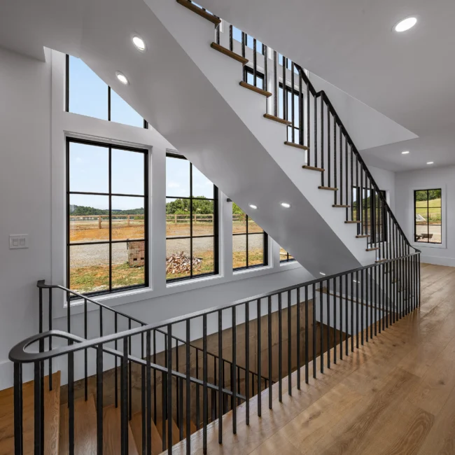 Staircase with black railing and windows overlooking countryside in Edgewater Estate, a custom home by Mike Stevens Homes