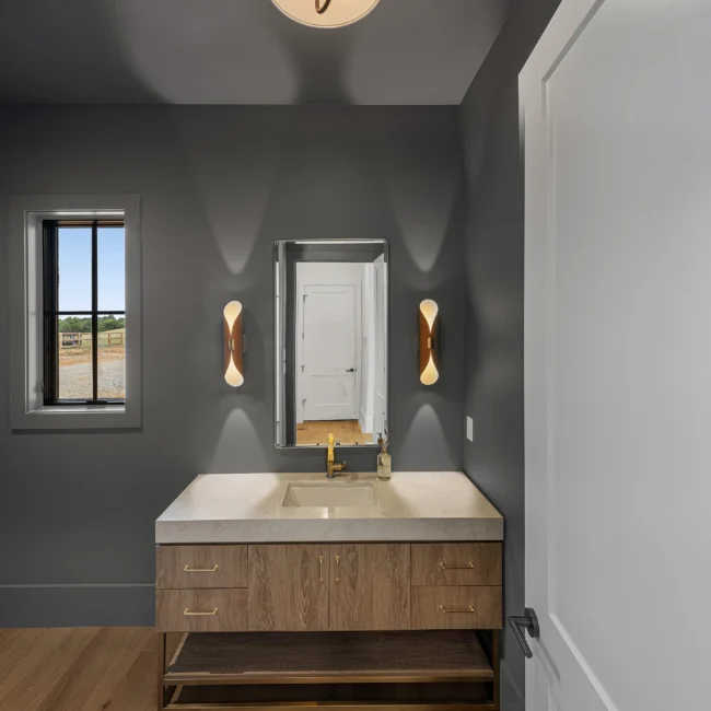 Powder room with gray walls, wood vanity and wall sconces in Edgewater Estate, a custom home by Mike Stevens Homes
