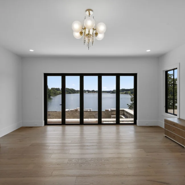 Empty room with black-framed glass doors overlooking the lake in Edgewater Estate, a custom home by Mike Stevens Homes