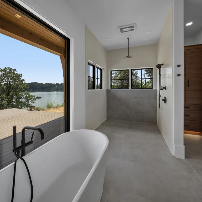 Freestanding tub by a lake-view window and walk-in shower in Edgewater Estate, a custom home by Mike Stevens Homes