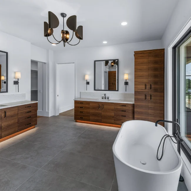 Primary bath with walnut vanities, toe-kick lighting and tub in Edgewater Estate, a custom home by Mike Stevens Homes