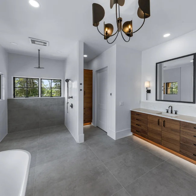 Primary bath with gray tile walk-in shower and walnut double vanity in Edgewater Estate, a custom home by Mike Stevens Homes