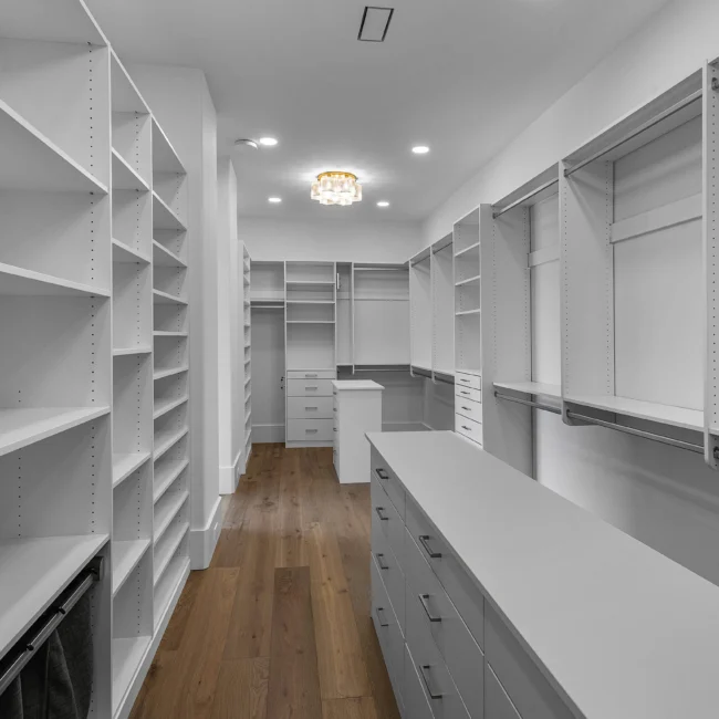 Walk-in closet with white built-in shelving and center island in Edgewater Estate, a custom home by Mike Stevens Homes