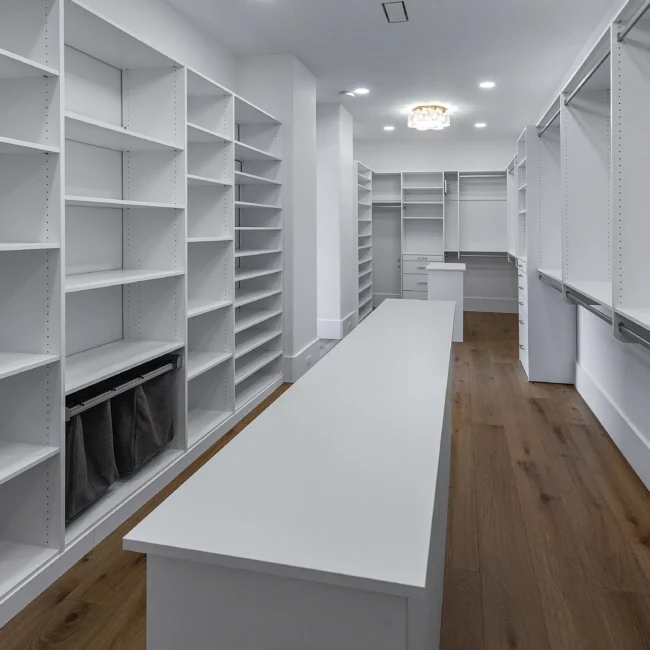 Walk-in closet with white shelving, hanging rods and center island in Edgewater Estate, a custom home by Mike Stevens Homes