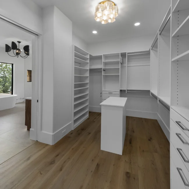 Walk-in closet with white built-ins, center island and wood floors in Edgewater Estate, a custom home by Mike Stevens Homes