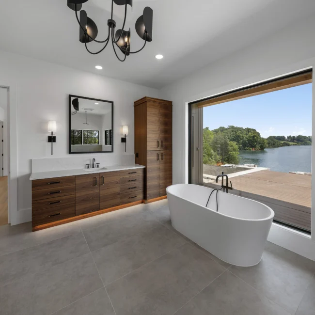Freestanding tub under a large window framing the lake in Edgewater Estate, a custom home by Mike Stevens Homes