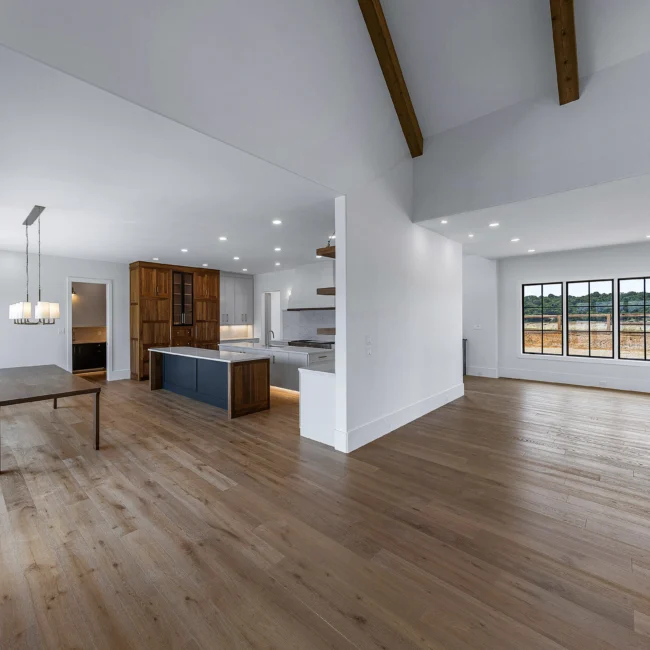 Open great room with timber beams and gray kitchen island in view in Edgewater Estate, a custom home by Mike Stevens Homes