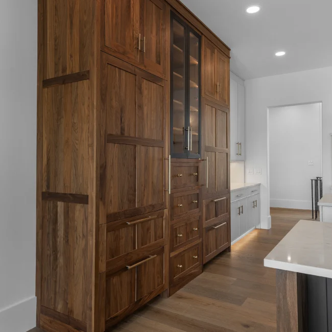 Tall walnut cabinetry with glass-front doors beside a kitchen in Edgewater Estate, a custom home by Mike Stevens Homes