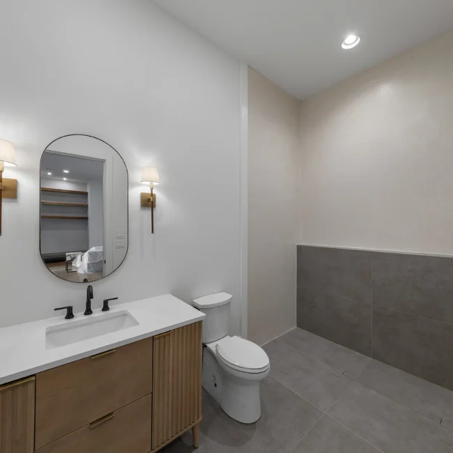Powder bath with oval mirror, sconces and dark vanity in Edgewater Estate, a custom home by Mike Stevens Homes