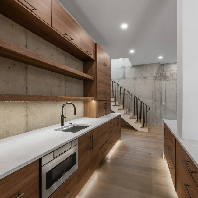Walnut kitchen with floating shelves, concrete wall and staircase in Edgewater Estate, a custom home by Mike Stevens Homes