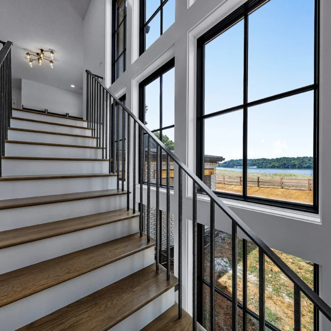 Open-tread staircase with black railings beside tall windows in Edgewater Estate, a custom home by Mike Stevens Homes
